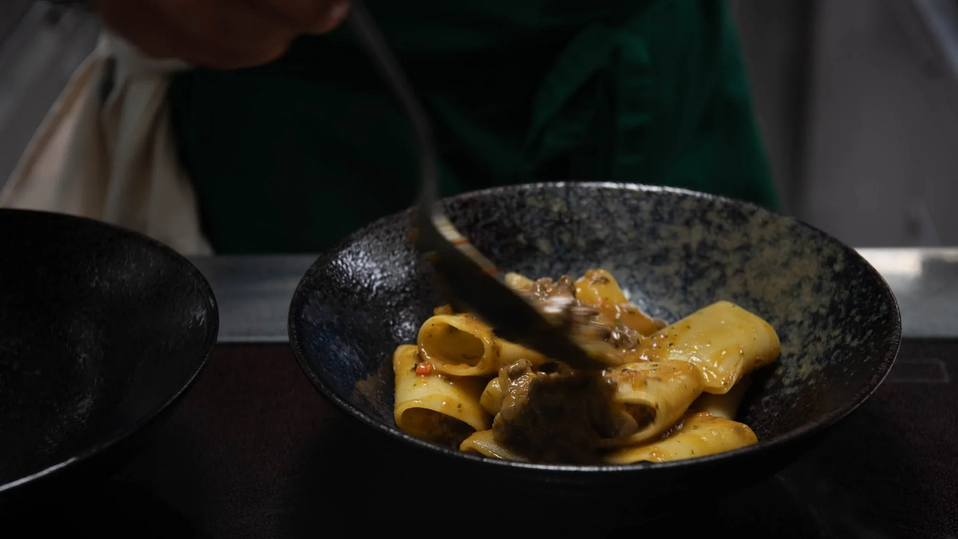 Küchenchef richtet Paccheri mit Ragout in dunkler, cineastischer Atmosphäre an