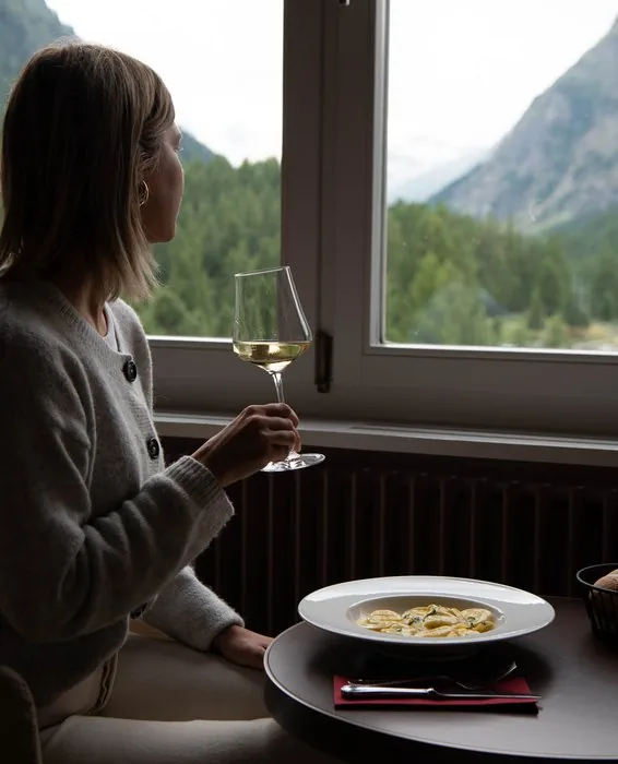 Gast geniesst Weisswein am Fenster mit Blick auf die Berge