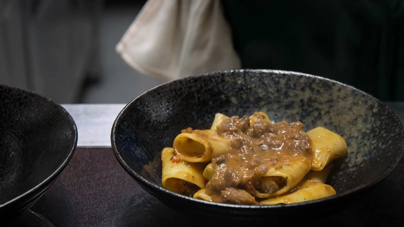 Der Koch richtet das Signature Dish an: Paccheri mit Ragout, in einer dunklen Keramikschale